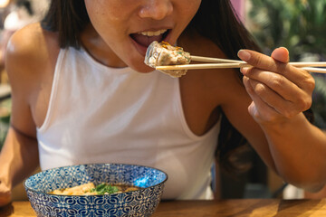Close up of smiling woman eating asian food with chop sticks