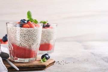 Chia strawberry pudding. Healthy vegan breakfast chia seeds pudding with fresh berries and mint in glass on gray concrete background. Concept of healthy eating, dieting, fitness menu. Selective focus.