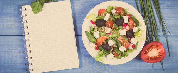 Fresh greek salad with feta cheese and notepad for notes. Healthy nutrition