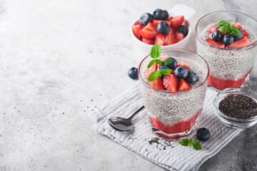 Chia strawberry pudding. Healthy vegan breakfast chia seeds pudding with fresh berries and mint in glass on gray concrete background. Concept of healthy eating, dieting, fitness menu. Selective focus.