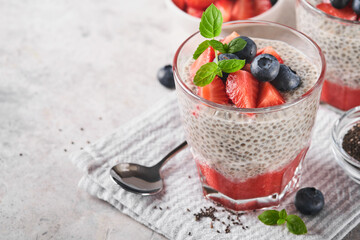 Chia strawberry pudding. Healthy vegan breakfast chia seeds pudding with fresh berries and mint in glass on gray concrete background. Concept of healthy eating, dieting, fitness menu. Selective focus.