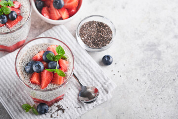 Chia strawberry pudding. Healthy vegan breakfast chia seeds pudding with fresh berries and mint in glass on gray concrete background. Concept of healthy eating, dieting, fitness menu. Selective focus.