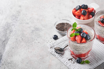 Chia strawberry pudding. Healthy vegan breakfast chia seeds pudding with fresh berries and mint in glass on gray concrete background. Concept of healthy eating, dieting, fitness menu. Selective focus.