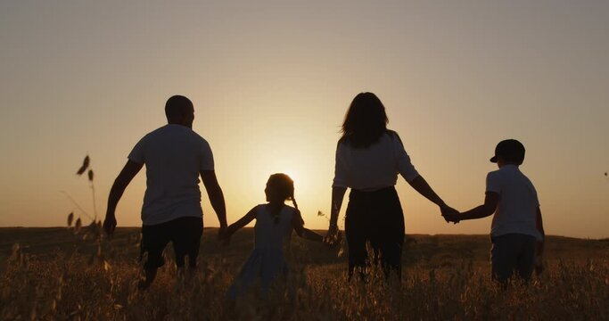 Happy family with children having fun jumping in the field at sunset