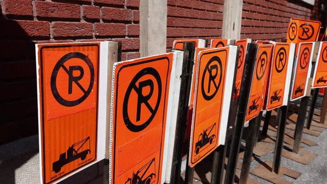 Camera panning in slow motion on a group of orange no parking signs stored against a red brick wall on a city center street in Montreal, Canada.