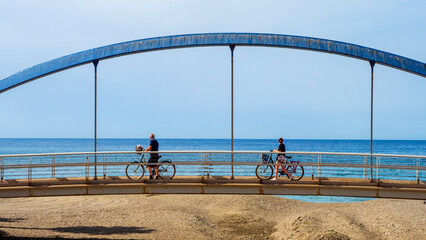 Pareja paseando en bicicleta sobre un puente frente al mar en Málaga