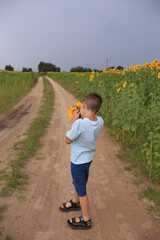 a child in a blue T-shirt stands with his back on the road and looks into the distance