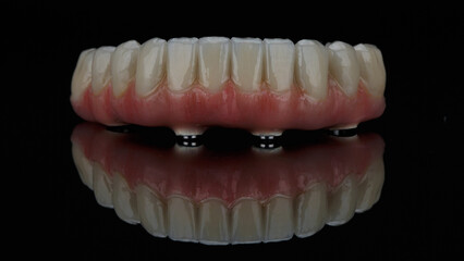 ceramic dental prosthesis of the lower jaw with natural gums on black glass with reflection