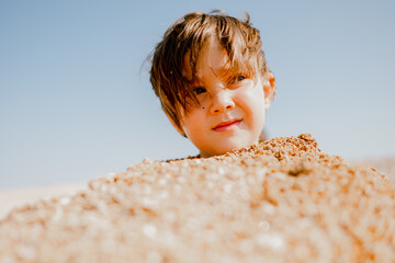 A happy toddler on the beach buried in the sand. Games on the beachBoy on the beach buried in the...