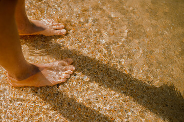 The boy wets his feet in the sea. Child in the summer on the beach