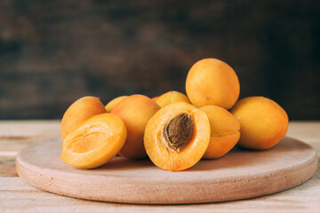 Apricots on a wooden kitchen board. Several ripe apricots, one of them cut in half.
