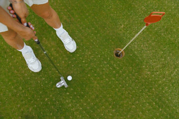 Woman holding golf club going to hit golf ball near hole, top view.