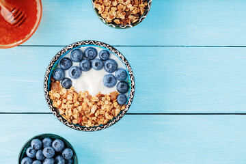 Yogurt with granola and blueberries on blue boards. Roasted granola with berries, yogurt and honey on the table. Top view. Copy space