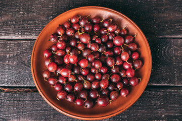 Top view of plate filled with ripe red gooseberries. Plate of berries in middle of table. Summer harvest.