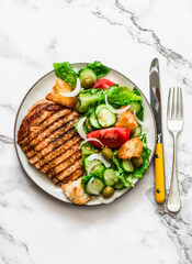 Grilled pork chop and Italian panzanella salad on a light marble background, top view