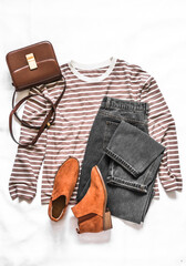 Women's clothing set - long sleeve striped pullover, crossbody bag, gray jeans, suede chelsea boots on a light background, top view