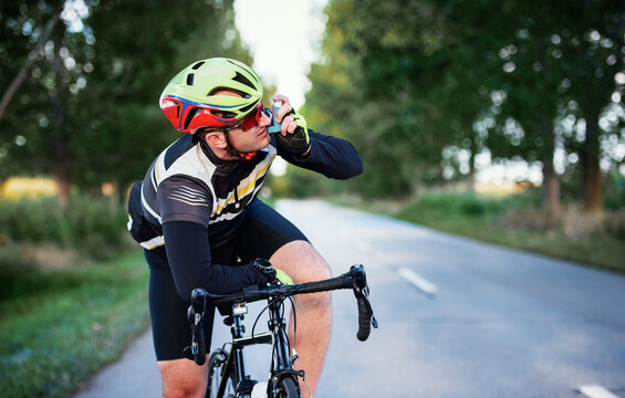 Sports and asthma. Cyclist using asthma inhaler while riding a bicycle. Sport and recreation concept