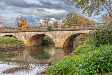 A view of the Melksham Town Bridge looking up river on an autumn day. The bridge on Bath Road crosses the River Avon and is a grade 2 listed structure of ashlar with arches and a balustraded parapet - obrazy, fototapety, plakaty