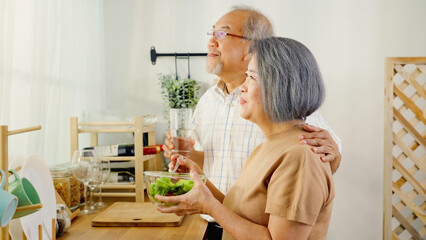 Asian senior grandparents are embracing and looking outside the window to enjoy the view together. Shot of the elderly retired couple are spending time together in the dining room enjoying breakfast.