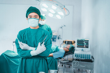 Portrait confidence doctor wear glove,medical mask stand arm cross hold sterile surgical instrument tool,equipment in operate room patient in background. Hospital, medical healthcare emergency concept