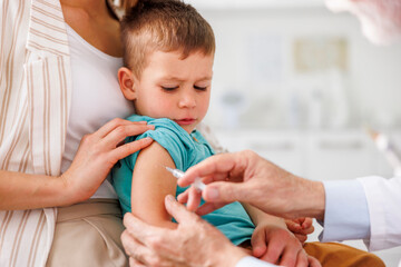 Mother holding son while he is being vaccinated by doctor at hospital
