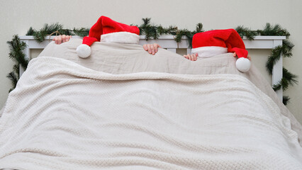 A man and a woman hid under a blanket on a bed decorated for Christmas and New Year in a home...