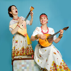 Women musicians in Russian folk dresses with musical instruments on a blue studio background. Happy...