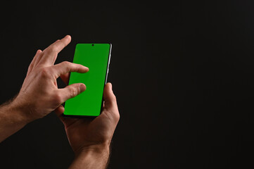 A man's hand holds a mobile phone with a green chrome screen. Use your fingers to zoom in on something on the screen. The concept of online shopping.