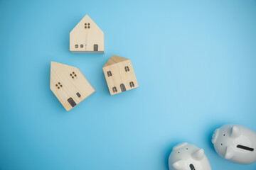 Top view of two white piggy banks with the wood of mini houses on blue background. Concept savings, investment, save money in future copy space. Finance, loan, saving money concept.