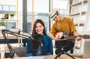 Fototapeta na wymiar Young couple in headset sing song play guitar streaming at real time on personal music channel at social media.Attractive couple sitting on sofa with a guitar.