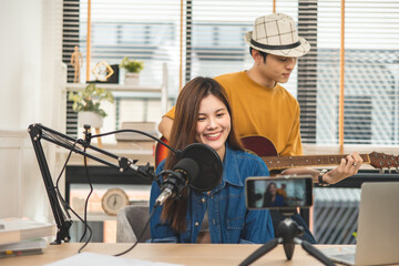 Young couple in headset sing song play guitar streaming at real time on personal music channel at...