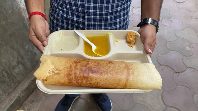Masala Dosa, a popular South Indian dish prepared of rice, lentils, potatoes, Methi, and curry leaves and served with chutneys and sambar, is being held in a man's hand. No face video