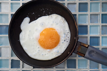 two 2 Fried salt eggs in skillet pan on blue checkered background close up, top view, breakfast food concept.