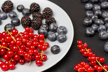 Berries of ripe red currants, blackberries and blueberries on gray plate and on table.