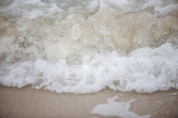 White sea waves spray with sand beach