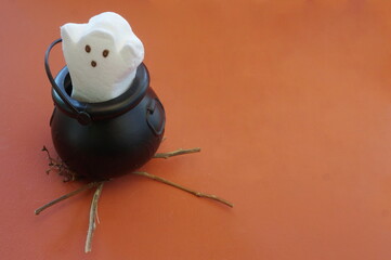 White Marshmallow Ghost Cooking in a Black Kettle on Orange Background 