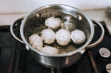 Chicken white large eggs are boiled in boiling water in a metal saucepan on the stove in the kitchen. Morning breakfast, food photography.