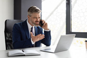 Stressed Middle Aged Businessman Talking On Cellphone And Using Laptop In Office