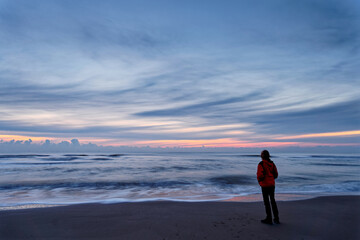 A woman standing by the ocean after sunset. Long exposure. North Holland dune reserve, Egmond aan Zee, Netherlands.