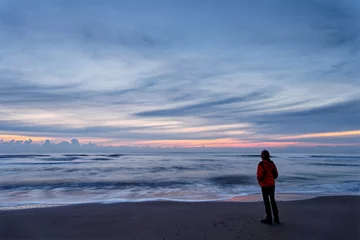 Fototapeten A woman standing by the ocean after sunset. Long exposure. North Holland dune reserve, Egmond aan Zee, Netherlands. © Susanne Fritzsche
