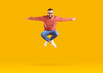 Fototapeta na wymiar Excited energetic young Caucasian man millennial jumping high with arms outstretched celebrating success or feeling joy after winning jackpot lottery posing in orange studio. Happiness from triumph