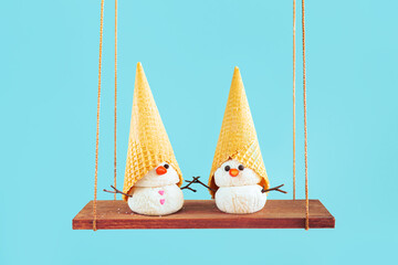 Two ice cream snowmen swing on a swing.