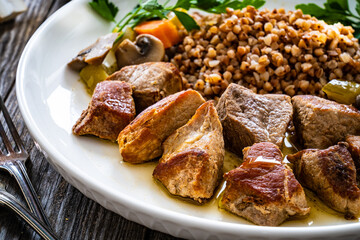 Roast pork with buckwheat groats, mushrooms and carrots served on wooden table
