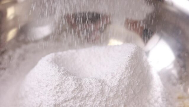 close up of sifting white flour or sugar powdered with sieve in steel bowl for pie, french dessert macarons or macaroons and cupcake making. slow motion. cooking desserts with sugar powder