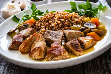 Roast pork with buckwheat groats, mushrooms and carrots served on wooden table
