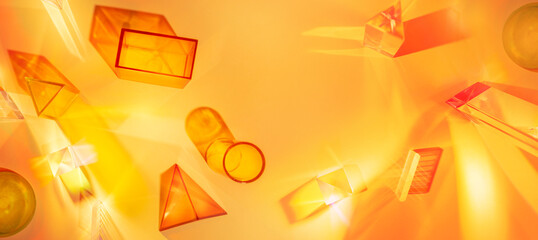 Abstract scene with geometric shapes and light rays on an orange-yellow background. Set of colored transparent geometric forms.