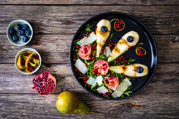 Fresh salad - prosciutto di Parma, pomegranate, pear, leafy vegetables and parmesan on wooden background