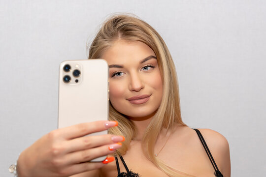A young and sexy girl of 20-25 years old takes a selfie on a smartphone on a white background. Concept: dating on the Internet, photos for social networks.