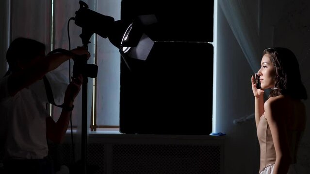 backstage, woman photographer takes pictures of a model in the studio who looks at the light on the silhouette