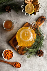 Obraz na płótnie Canvas Teapot with sea buckthorn tea. A warming winter drink. Vitamin tea. Sea buckthorn tea with honey, lemon and ginger on a gray background. Top view. 